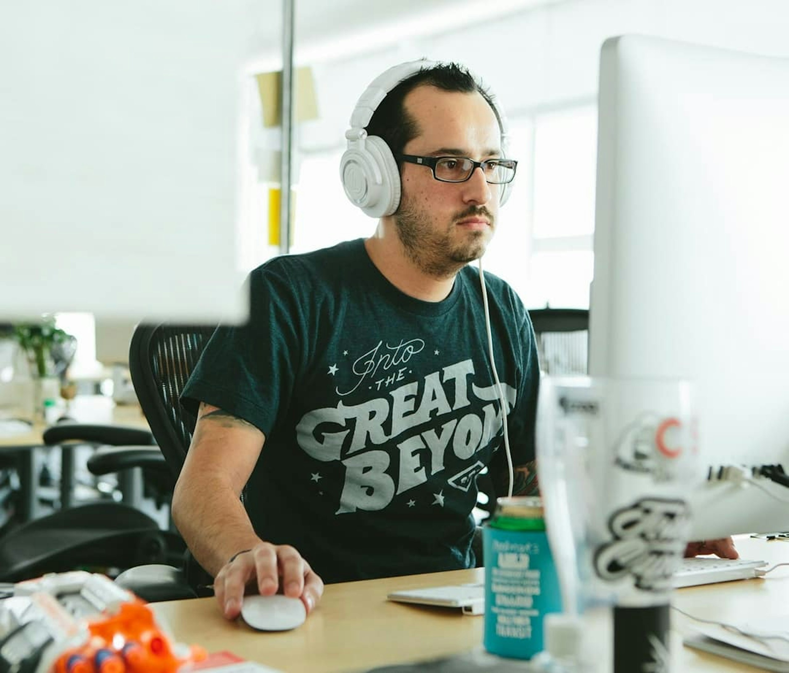 A man works at a desk wearing a custom t-shirt that says "into the great beyond"